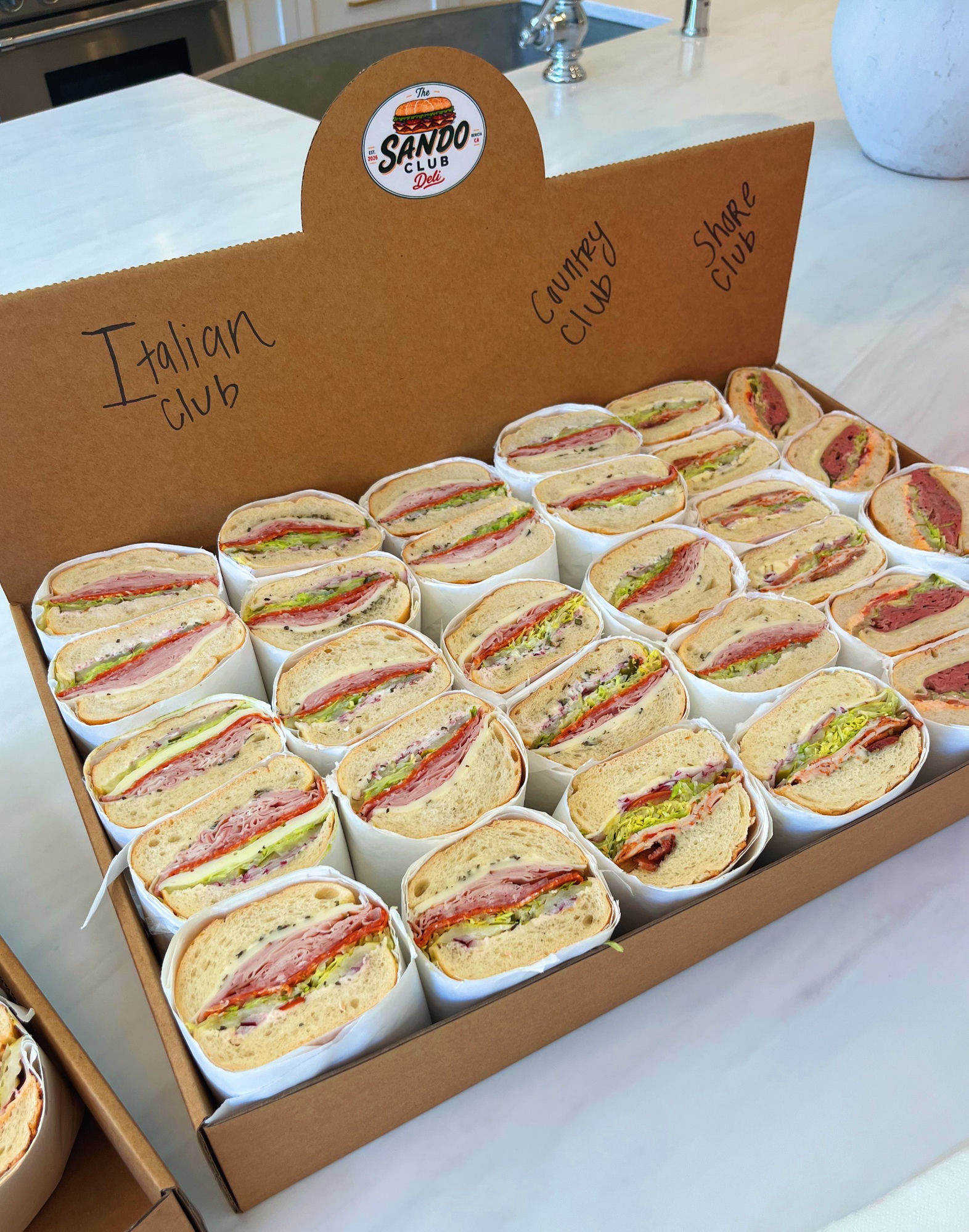 A Sando Club Deli catering box packed with individually wrapped Italian, Country, and Shore Club sandos